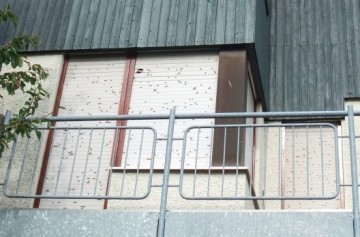 Einfamilienhaus mit durch Hagel beschädigtem Rollladen und Holzfassade